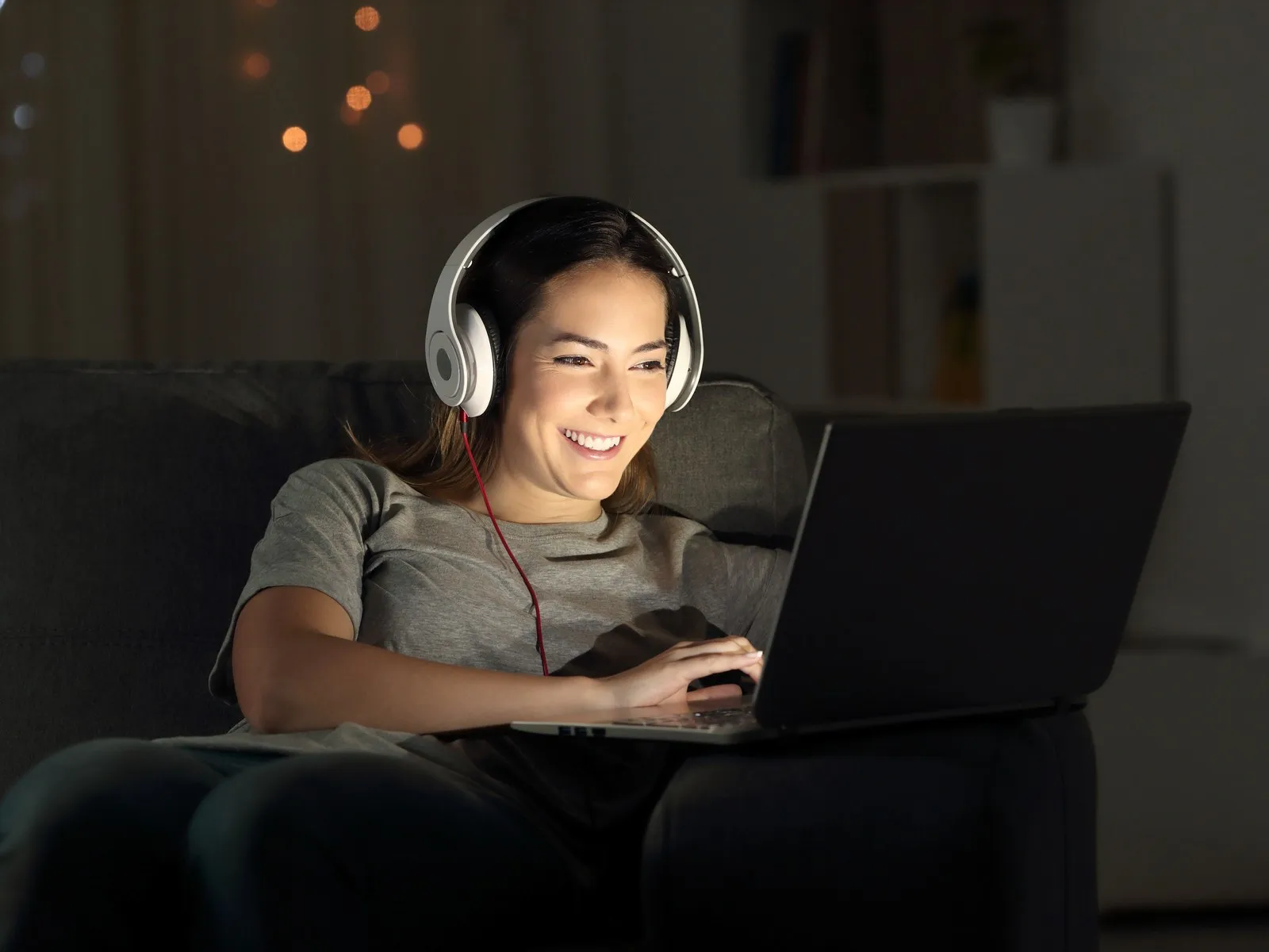 A woman watching a film on her laptop with headphones in the evening.
